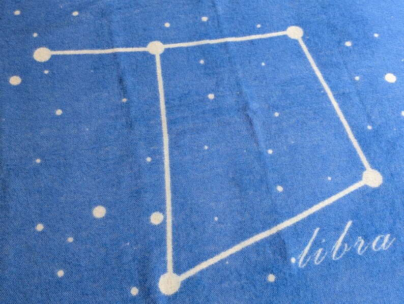 May include: A blue throw blanket with a white constellation design of Libra. The word "Libra" is written in white script in the bottom right corner.