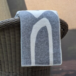 May include: A gray and white patterned throw blanket draped over the back of a wicker chair.