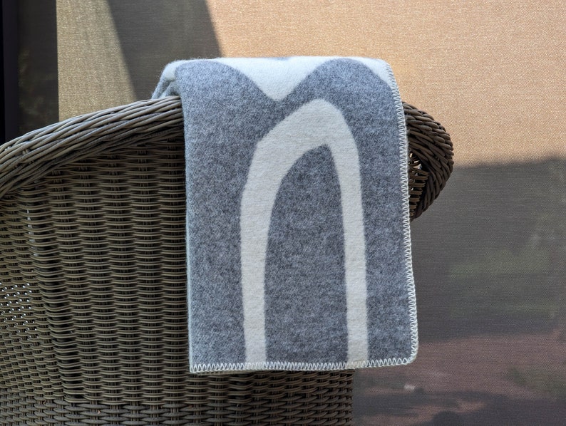 May include: A gray and white patterned throw blanket draped over the back of a wicker chair.