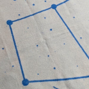 May include: A white fabric with a blue constellation pattern. The constellation is a square shape with five points.