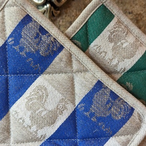Puede incluir: Dos agarraderas acolchadas, una azul y blanca y otra verde y blanca, con un patr&oacute;n de p&aacute;jaros estilizados.