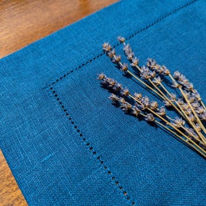 May include: A blue linen placemat with dried lavender sprigs on top.