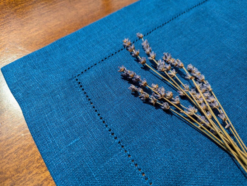 May include: A blue linen placemat with dried lavender sprigs on top.
