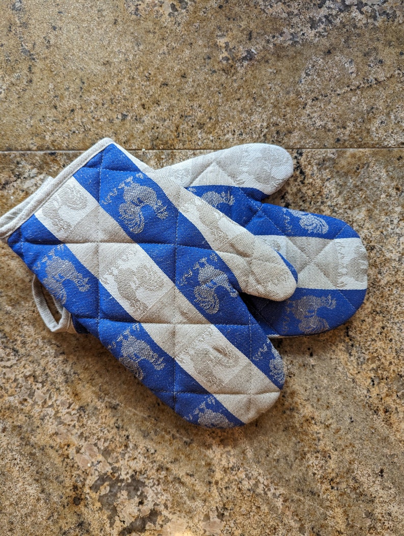 Puede incluir: Un par de guantes de horno a rayas azules y blancas con un dise&ntilde;o acolchado. Los guantes tienen un patr&oacute;n de gallos estilizados.