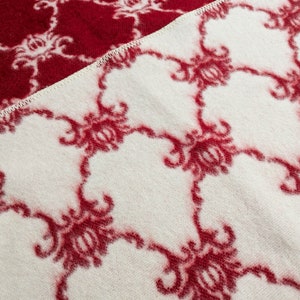 May include: A white blanket with a red floral pattern. The blanket is made of a soft, fuzzy material.