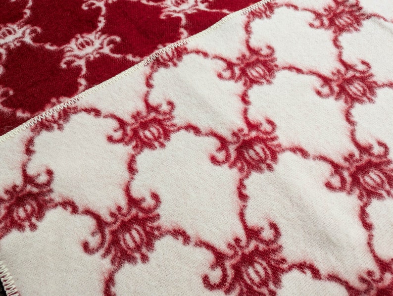May include: A white blanket with a red floral pattern. The blanket is made of a soft, fuzzy material.