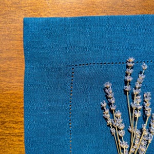 May include: A blue linen napkin with a sprig of dried lavender on top.