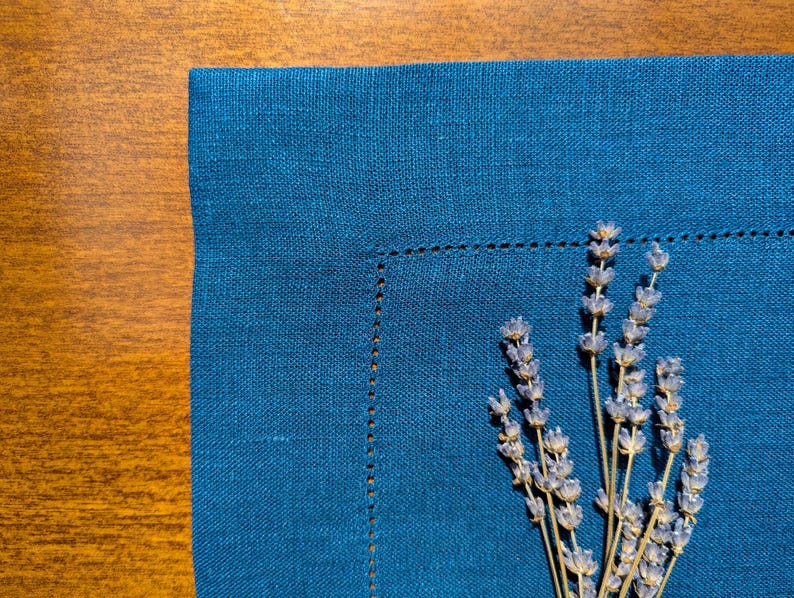 May include: A blue linen napkin with a sprig of dried lavender on top.