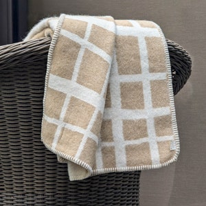 May include: A beige and white patterned throw blanket draped over the back of a wicker chair.