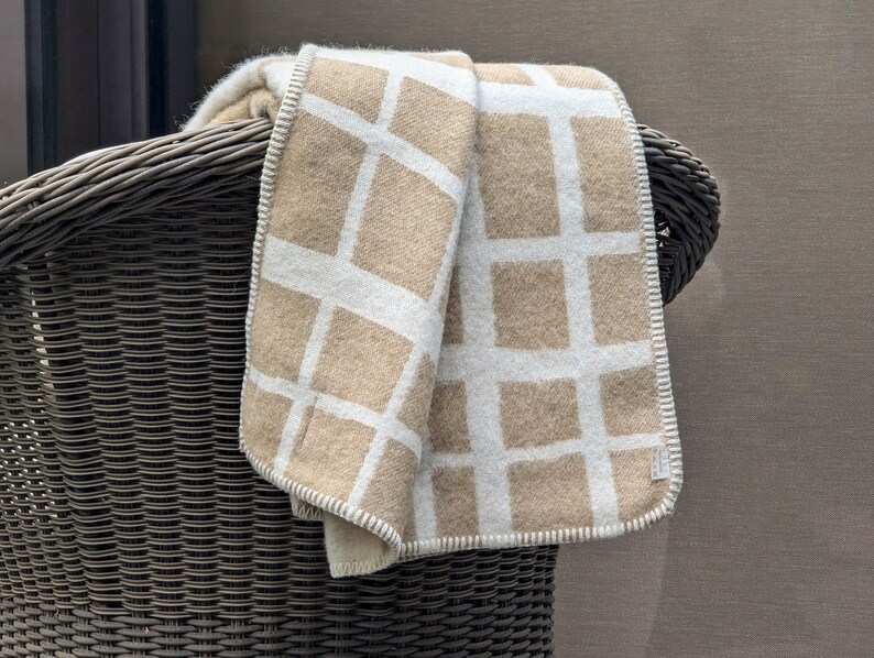 May include: A beige and white patterned throw blanket draped over the back of a wicker chair.