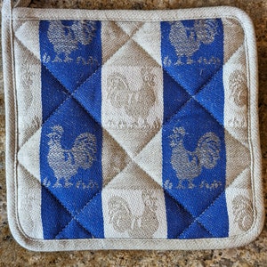 Puede incluir: Un posavasos acolchado azul y blanco con un dise&ntilde;o de gallo. El gallo est&aacute; bordado en hilo plateado y el texto "La Ferme" est&aacute; impreso en azul.
