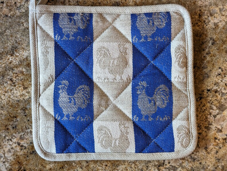 Puede incluir: Un posavasos acolchado azul y blanco con un dise&ntilde;o de gallo. El gallo est&aacute; bordado en hilo plateado y el texto "La Ferme" est&aacute; impreso en azul.