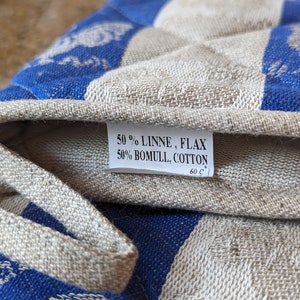 Puede incluir: Primer plano de un agarrador de olla a rayas azules y blancas con una etiqueta blanca que dice "50% LINNE, FLAX 50% BOMULL, COTTON 60 C".