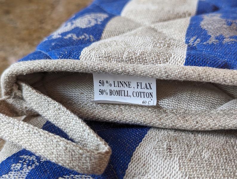 Puede incluir: Primer plano de un agarrador de olla a rayas azules y blancas con una etiqueta blanca que dice "50% LINNE, FLAX 50% BOMULL, COTTON 60 C".