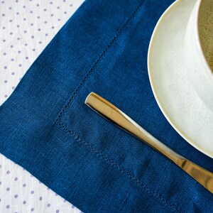 Puede incluir: Un mantel individual de lino azul sobre un mantel blanco con lunares blancos. Un cuchillo de plata est&aacute; sobre el mantel individual. Un cuenco de cer&aacute;mica blanca con superficie texturizada est&aacute; sobre el mantel.