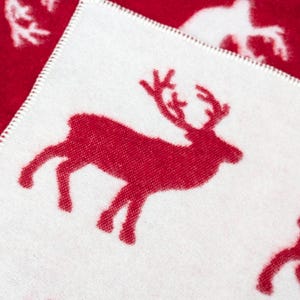 May include: White fabric with a red reindeer silhouette design. The reindeer is facing right and has a large, curved antler.