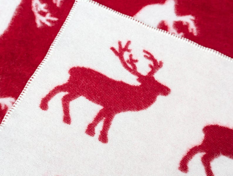 May include: White fabric with a red reindeer silhouette design. The reindeer is facing right and has a large, curved antler.