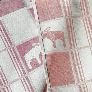 Puede incluir: Una toalla de cocina a cuadros rosa y blanca con un dise&ntilde;o de alce. La toalla est&aacute; hecha de un tejido suave y absorbente, ideal para secar platos o limpiar derrames.