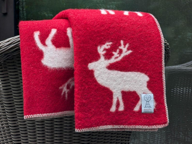 May include: Red wool throw blanket with a white reindeer design. The blanket has a white border and a small white tag with the text "Made in Scotland" on it.