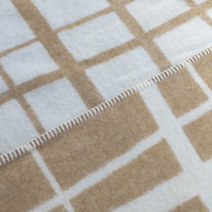 May include: A white and brown woven blanket with a checkered pattern. The blanket has a stitched edge.