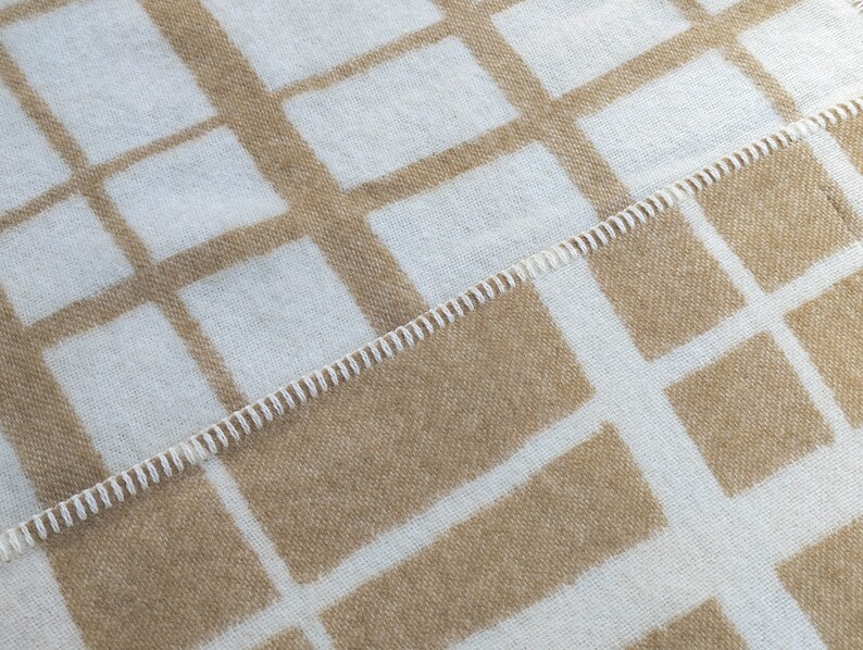 May include: A white and brown woven blanket with a checkered pattern. The blanket has a stitched edge.