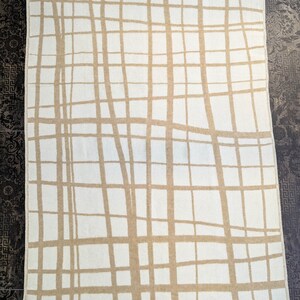 May include: A white throw blanket with a tan grid pattern. The blanket has a woven texture and a fringed edge.
