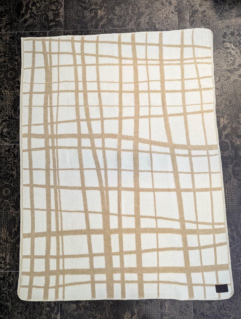 May include: A white throw blanket with a tan grid pattern. The blanket has a woven texture and a fringed edge.
