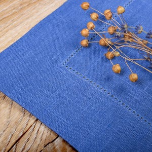 May include: A blue linen placemat with a decorative stitch pattern and dried flowers on top.