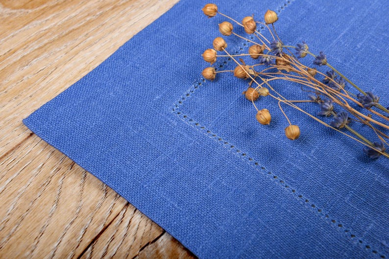 May include: A blue linen placemat with a decorative stitch pattern and dried flowers on top.