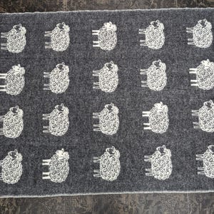 May include: A gray wool throw blanket with a white sheep design. The blanket has fringe on all sides.