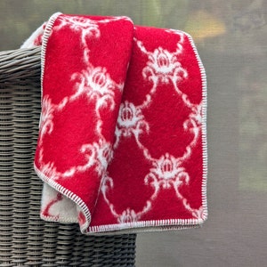 May include: A red and white patterned blanket folded over a wicker basket. The blanket has a white floral design on a red background.