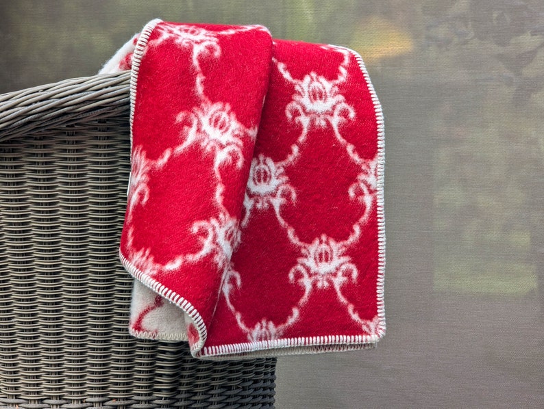 May include: A red and white patterned blanket folded over a wicker basket. The blanket has a white floral design on a red background.
