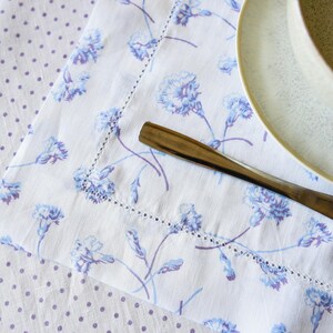 May include: A white table runner with a blue floral pattern and a white polka dot tablecloth underneath. A silver fork is placed on the table runner.
