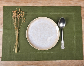 May include: A green linen placemat with a white ceramic plate and a silver spoon on top.