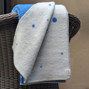 May include: A white and blue throw blanket with a blue polka dot pattern. The blanket is folded and draped over a wicker chair.