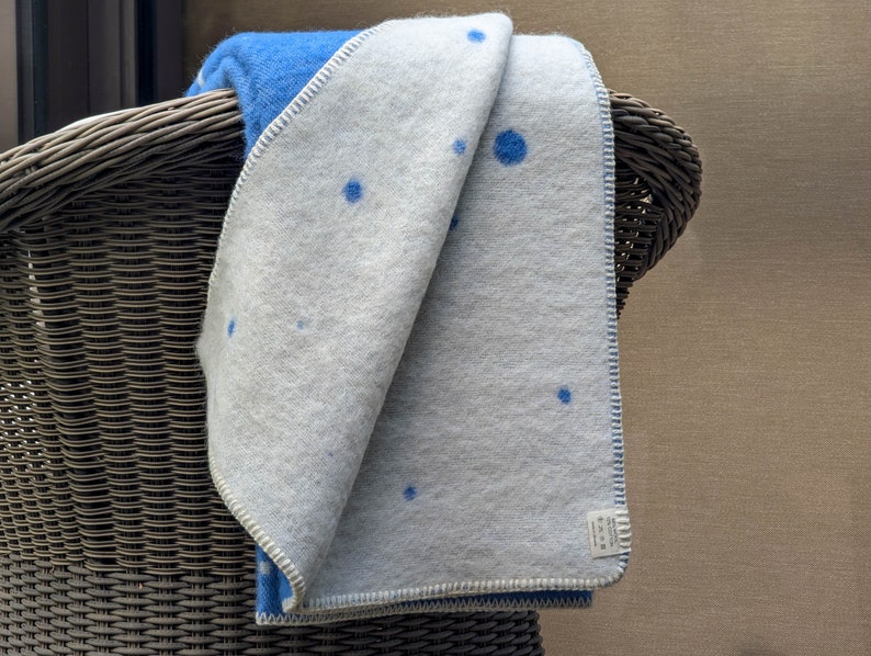 May include: A white and blue throw blanket with a blue polka dot pattern. The blanket is folded and draped over a wicker chair.