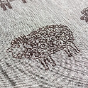 May include: A white fabric with a repeating pattern of brown sheep. The sheep are stylised and have a curly wool design.