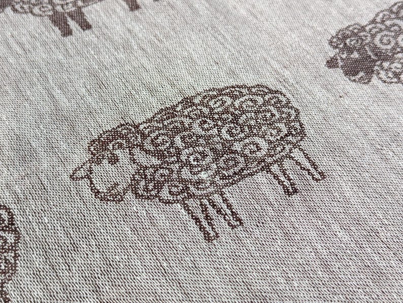 May include: A white fabric with a repeating pattern of brown sheep. The sheep are stylised and have a curly wool design.