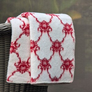 May include: A white throw blanket with a red floral pattern. The blanket is folded and draped over a wicker chair.