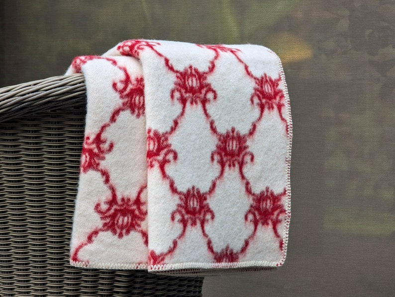 May include: A white throw blanket with a red floral pattern. The blanket is folded and draped over a wicker chair.