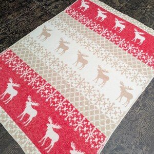 May include: A red and cream throw blanket with a repeating pattern of snowflakes and moose. The blanket is made of a soft, fuzzy material.