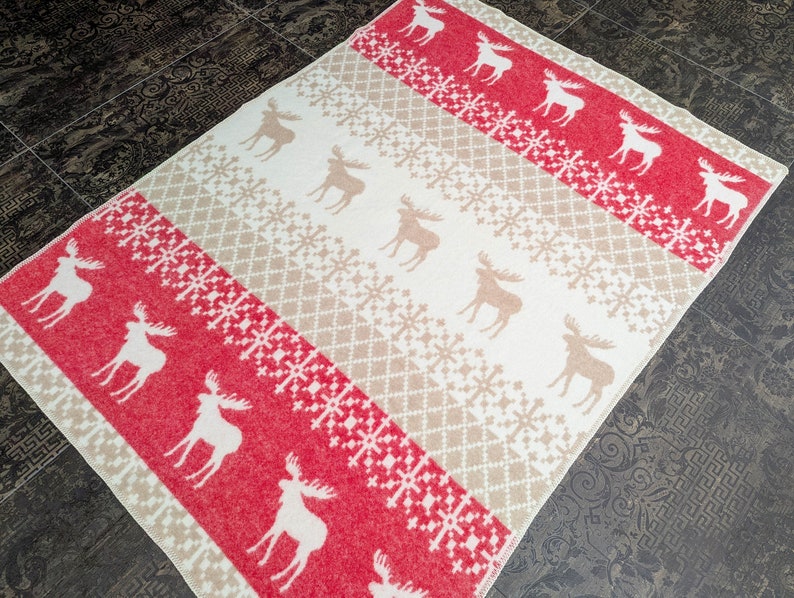 May include: A red and cream throw blanket with a repeating pattern of snowflakes and moose. The blanket is made of a soft, fuzzy material.