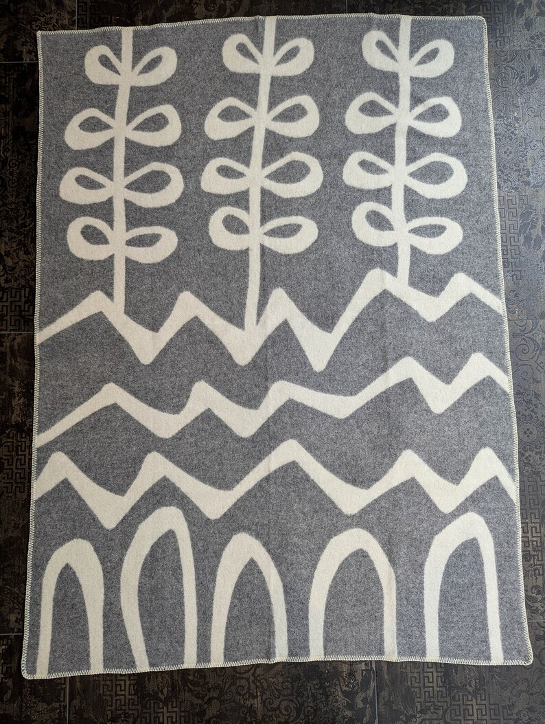 May include: A gray and white wool throw blanket with a geometric pattern of stylized plants, waves, and arches.