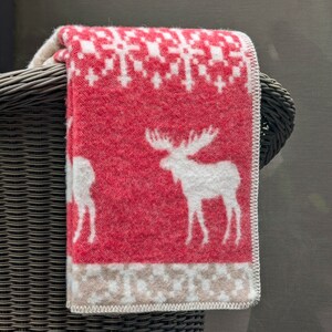 May include: A red and white patterned throw blanket with a white moose design. The blanket is folded and draped over a wicker chair.