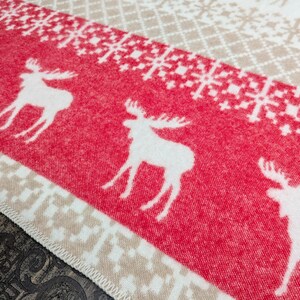 May include: A red and white patterned throw blanket with a white moose design. The blanket has a beige border.
