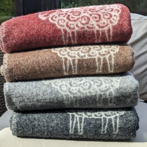 May include: A stack of four wool blankets with a sheep design. The blankets are in shades of red, brown, gray, and black.