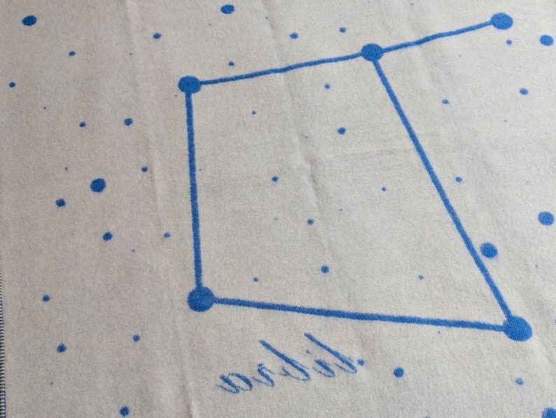 May include: A white throw blanket with a blue constellation design and the word "wobbly" written in cursive.