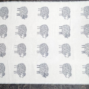 May include: White throw blanket with a repeating pattern of gray sheep. The sheep are stylized with curly wool and have four legs.