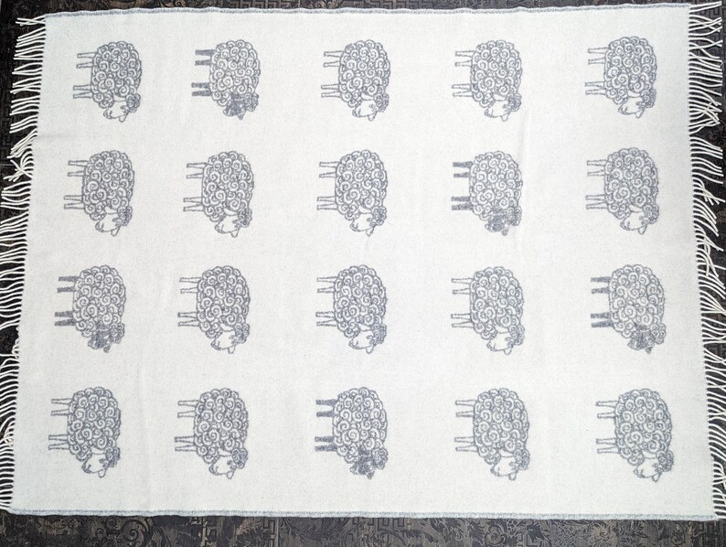 May include: White throw blanket with a repeating pattern of gray sheep. The sheep are stylized with curly wool and have four legs.