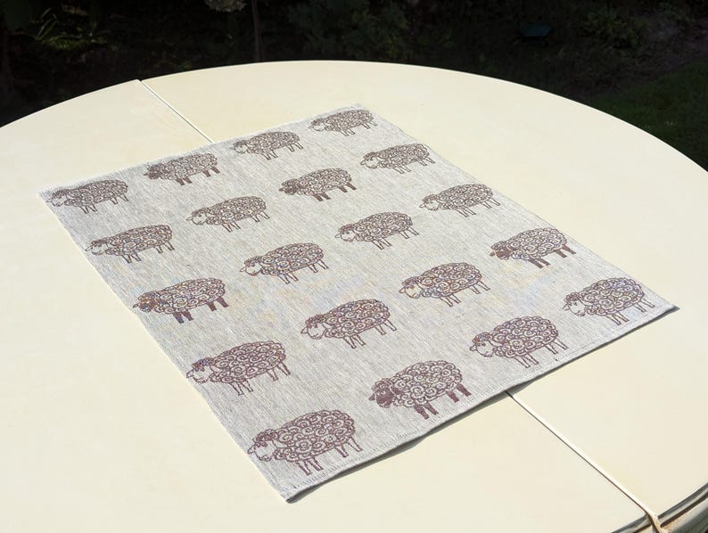 May include: A light grey linen table runner with a repeating pattern of brown sheep. The sheep are stylised and have curly wool.